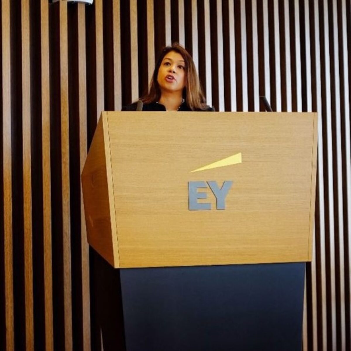Tulip Siddiq delivering a speech at an EY podium